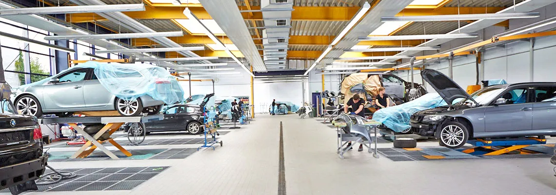 Das Bild zeigt die Vorbereitungshalle für das Lackieren. Es sind mehrere Autos mit Plastikfolie abgeklebt.