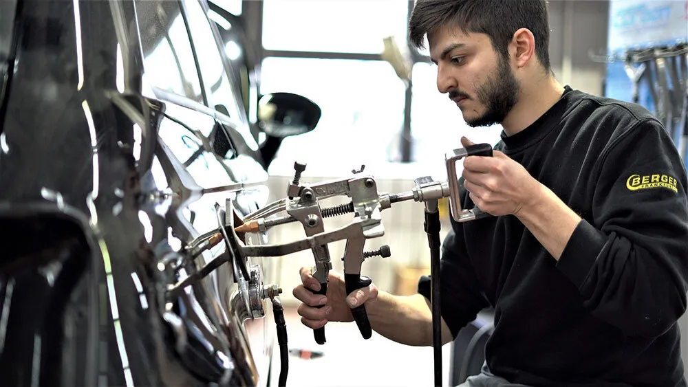 Ein Mitarbeiter wendet ein Spezialwerkstatt für das Smart Repair um eine Delle zu entfernen an einer Autotür an.